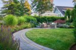 A winding path leads to a table and chairs. A little girl walks by.